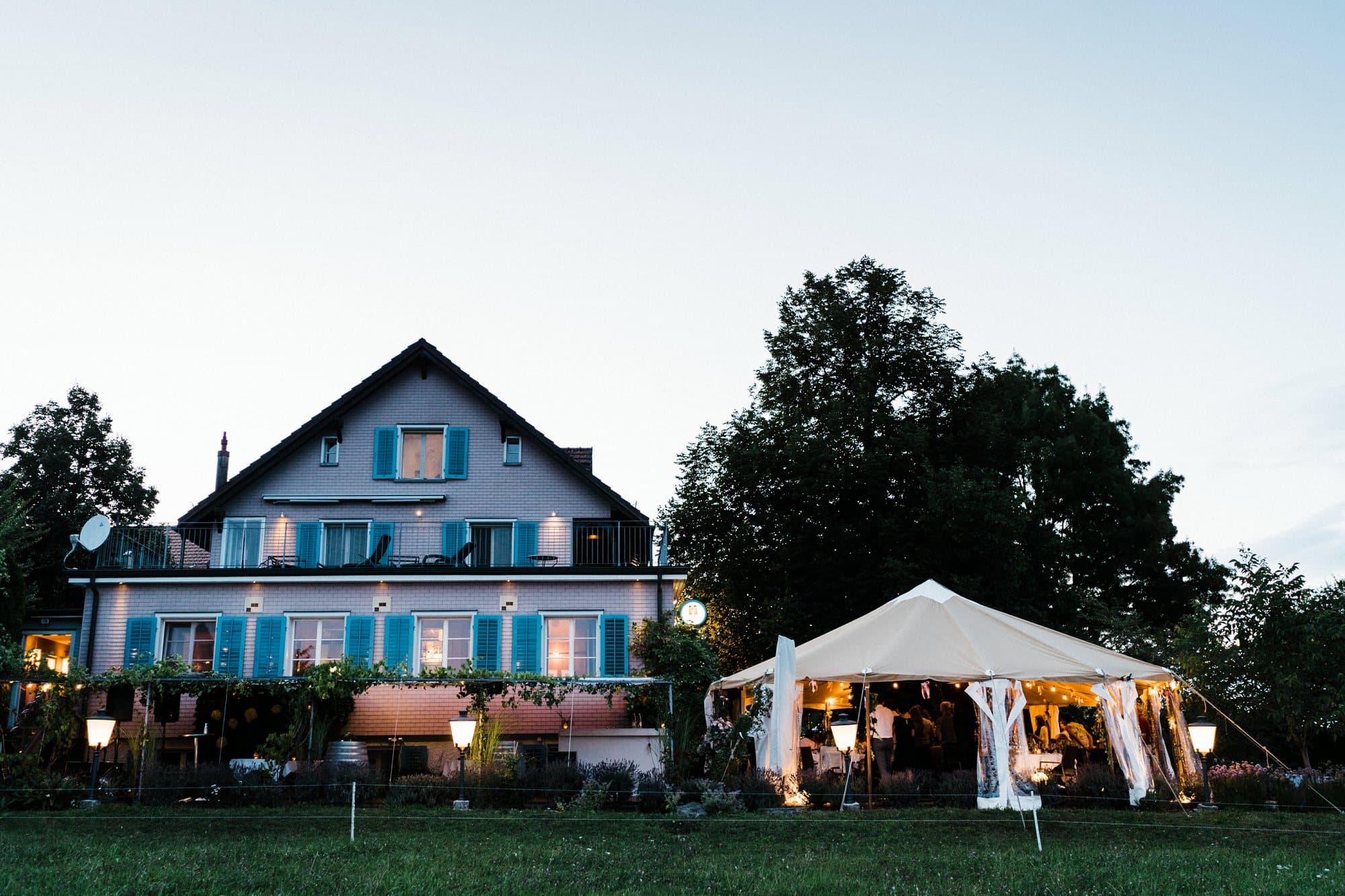 Beleuchtetes Zelt neben einem Bauernhaus bei einer Hochzeit am Abend