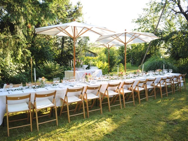Lange gedeckte Tafel mit Holzstühlen und Sonnenschirmen im Garten